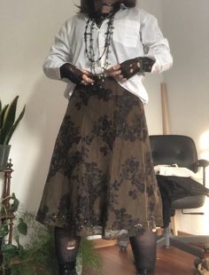 A mid-size person/girl wearing a closed wide white button up with a black ripped tights longsleeve under it, a dark green flower midi skirt, rose patterned stockings,  black platform dr. Martens and multiple crystal rings and bracelets. 	The person is also wearing multiple silver necklaces; one in form of a moon, a butterfly, and one in form of a fairy, a long black and green bead necklace and a green buttery choker. Cottagecore Pirate Aesthetic, Goblincore Skirts, Moss Aesthetic Outfit, Earth Goth Aesthetic, Masc Skirt Outfit, Pirate Cottagecore, Thrifting Aesthetic Outfits, Earth Goth, Pirate Aesthetic Outfit