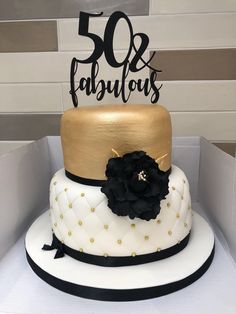 a white and gold cake with black flowers on top is sitting in a box next to a sign that says 50 and fabulous