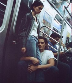 two people sitting on a subway train next to each other and one person leaning against the wall