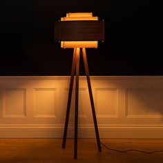 a lamp that is sitting on top of a wooden tripod in front of a wall