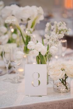 the table is set up with white flowers and place cards for guests to sit at