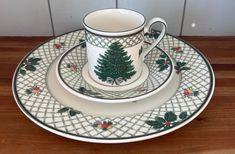 a set of christmas dishes with a tree on the front and side, sitting on a wooden table