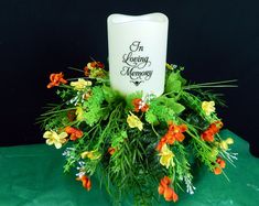 a candle that is sitting on top of a green cloth with flowers and greenery around it