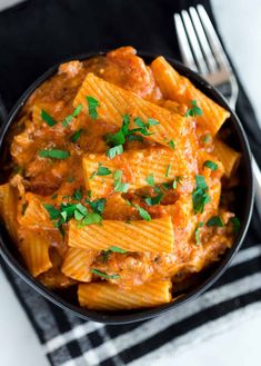 a bowl filled with pasta and sauce on top of a black cloth next to a fork