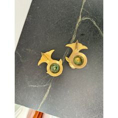 pair of gold earrings with green stones on black marble counter top next to orange vase