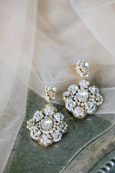 a pair of gold and crystal earrings on a white cloth background with sheer fabric behind it