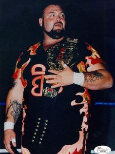 a man with tattoos on his arms and chest standing in front of a wrestling ring