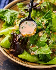 a bowl filled with lettuce and dressing on top of a wooden table next to a fork