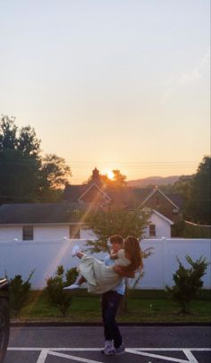 a woman holding a baby in her arms while standing next to a parked car at sunset