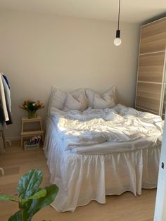 an unmade bed sitting in a bedroom next to a plant