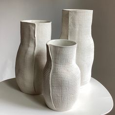 three white vases sitting on top of a white plate next to eachother