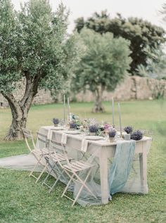 an outdoor table set up with chairs and flowers on it in the middle of a field