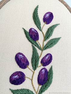 a close up of a embroidery on a piece of cloth with purple flowers and green leaves