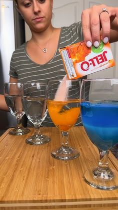 a woman is pouring blue liquid into three glasses on a counter top with orange and blue liquids in them