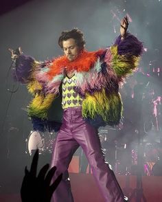 the man is dressed in colorful clothing and holding his arms out as he stands on stage