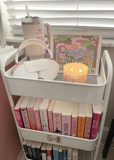 a book shelf filled with books and a lit candle on top of it next to a window