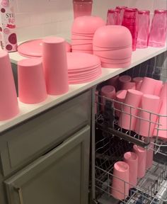 many pink cups and plates are stacked on the shelf in front of the dishwasher