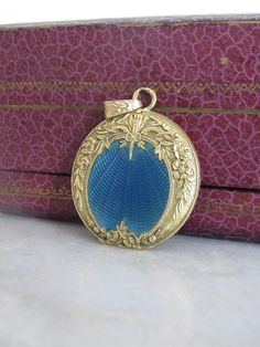 I'm so pleased to offer this exceptional antique locket crafted in the Belle Epoque style around 1910. This breathtaking round pendant boasts finely decorate floral chasing which frames translucent blue enamel over meticulous engine turned engraving.  A delicate process, enamel is made by fusing powdered glass to metal surfaces through a high-temperature firing process. The intense heat melts the glass powder, allowing it to adhere to the metal and form a smooth, glossy coating; the vitreous gla Victorian Style Medallion Locket Necklace With Filigree, Antique Round Pendant Locket Necklace With Intricate Design, Antique Round Pendant Locket Necklace For Formal Occasions, Victorian Medallion Locket Necklace With Filigree, Victorian Style Filigree Medallion Locket Necklace, Victorian Style Round Filigree Locket Necklace, Antique Locket Necklace With Intricate Round Pendant, Victorian Locket Necklace With Intricate Round Pendant, Victorian Filigree Medallion Locket Necklace