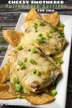 chicken enchiladas with cheese and green onions on a white plate next to tortilla chips