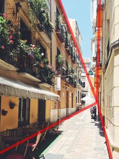 a narrow street with tables and chairs lined up along the side of it, in front of tall buildings