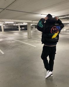 a man in a parking garage talking on a cell phone and wearing a jacket with the word love written on it