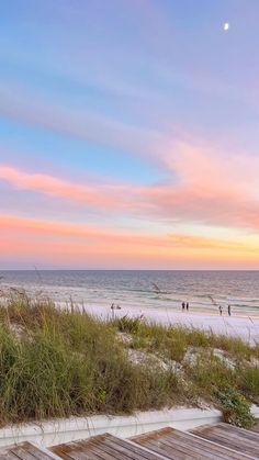 an empty beach with people walking on the sand and water in the background at sunset