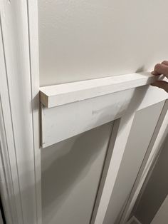 a person is holding the door handle on a white door with wood trimmings