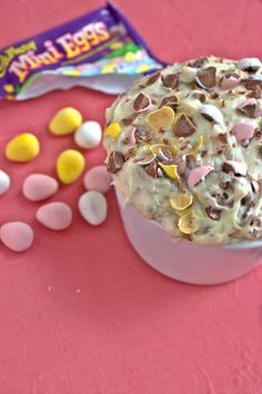 a cup filled with candy and marshmallows on top of a pink table