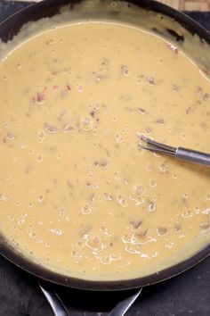 a skillet filled with soup on top of a wooden table next to two spoons