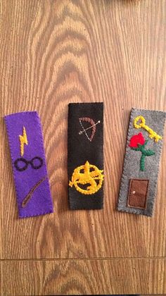 three bookmarks with different designs on them sitting on top of a wooden table next to a pair of glasses