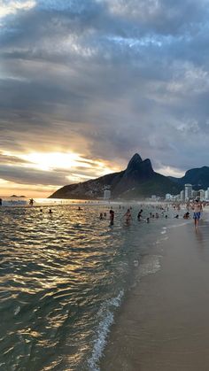 many people are swimming in the water at sunset on a beach with mountains in the background