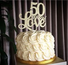 a 50th birthday cake with white frosting and gold decorations on top, sitting on a table