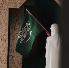 a person holding a green flag in front of a wall with arabic writing on it