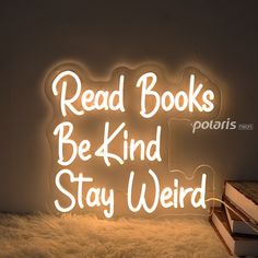 a neon sign that reads read books be kind stay weird on top of a pile of books