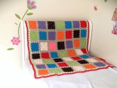 a crocheted blanket sitting on top of a bed next to a flowered wall