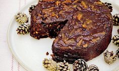 a piece of chocolate cake on a white plate with pine cones and nuts around it