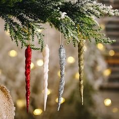 christmas ornaments hanging from a tree with lights in the background