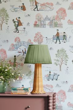 a lamp sitting on top of a dresser next to a wallpaper covered in trees