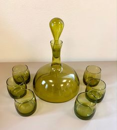 a green glass vase sitting on top of a table next to glasses and a pitcher