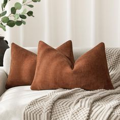 two brown pillows sitting on top of a white couch next to a potted plant