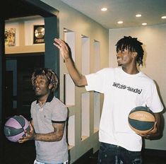 two young men holding basketballs standing next to each other in front of a wall