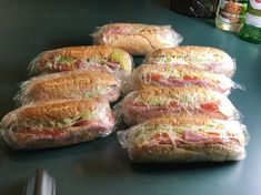 sandwiches wrapped in plastic sitting on top of a counter next to bottles of sodas