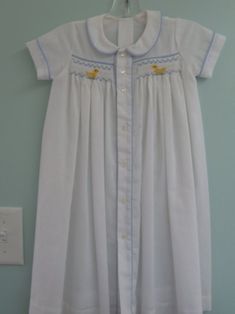 a baby's white and blue dress hanging on a wall next to a light switch