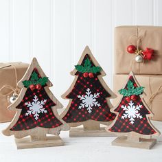 three small wooden christmas trees with snowflakes on them and presents in the background