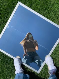 a person standing in front of a mirror on the grass with their feet up and one hand holding a cell phone