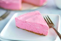 a piece of pink cheesecake on a plate with a fork and cup in the background