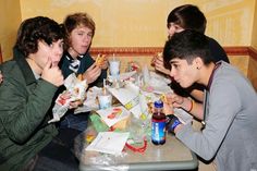 four boys sitting at a table eating food