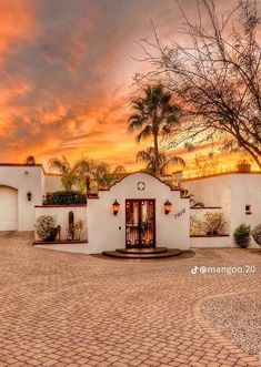 an adobe style home sits in the middle of a driveway with potted plants on either side