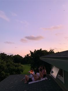 three women sitting on the roof of a house at sunset, drinking wine and talking