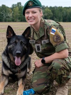 a woman in uniform kneeling next to a german shepherd dog on the ground with her tongue hanging out